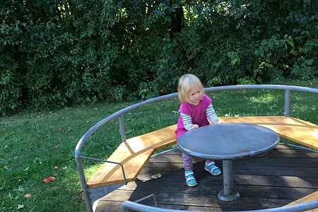 Kleines Mädchen sitzt im Rondell und zieht an dem Innentisch, denn dann bewegt sich das Rondell.