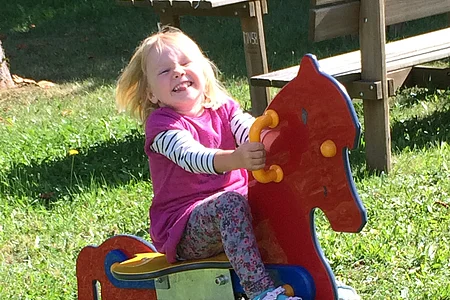 Junges Mädchen hat mächtig Spaß auf dem bunten Wipppferd.