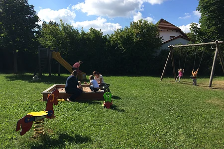 Kinder spielen im Sandkasten oder lassen sich auf der Schaukel treiben.